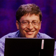 A photograph of Bill Gates smiling while working on a laptop.